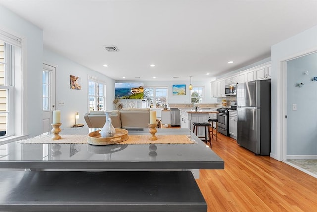 kitchen with white cabinetry, a center island, stainless steel appliances, light hardwood / wood-style floors, and a breakfast bar area