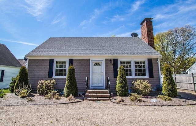 bungalow-style house with a shingled roof, fence, and a chimney