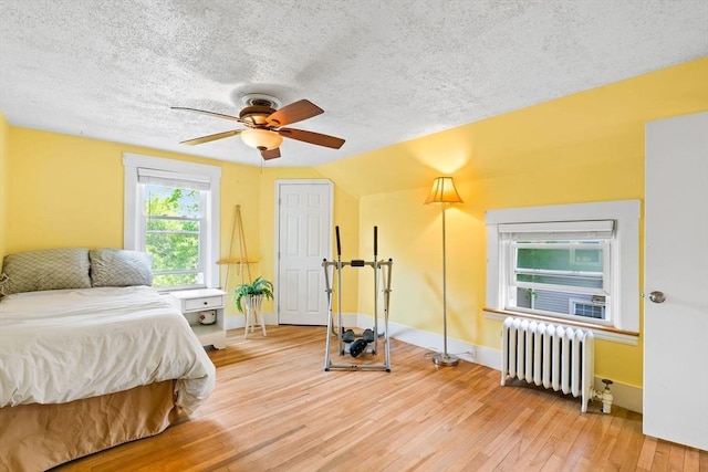 112 Lawrence St, Fitchburg, MA 01420 - bedroom with radiator heating unit, light wood-style floors, a textured ceiling, baseboards, and a ceiling fan