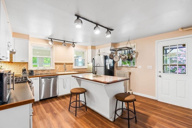 112 Lawrence St, Fitchburg, MA 01420 - kitchen with appliances with stainless steel finishes, a sink, white cabinets, a breakfast bar, and wood finished floors