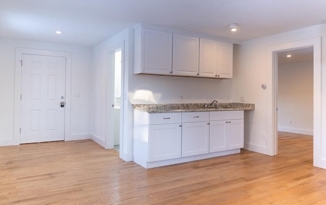 kitchen featuring light stone counters, sink, white cabinets, and light wood-type flooring