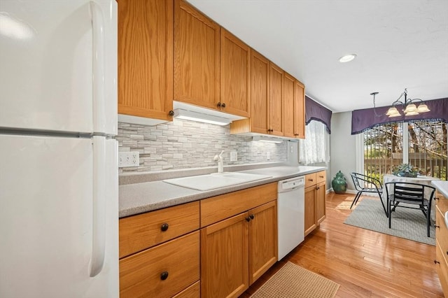 kitchen featuring white appliances, decorative backsplash, light wood-style floors, light countertops, and a sink