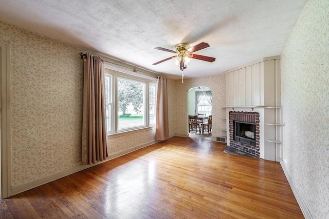 405 Granby Rd, South Hadley, MA 01075 - unfurnished living room with wallpapered walls, wood finished floors, arched walkways, a ceiling fan, and a brick fireplace