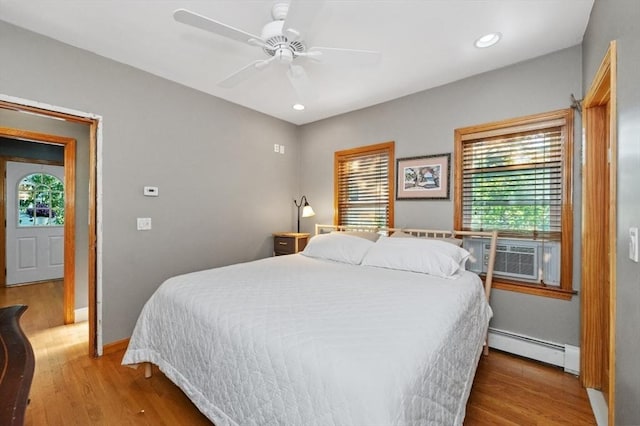 bedroom featuring a baseboard heating unit, cooling unit, baseboards, and wood finished floors