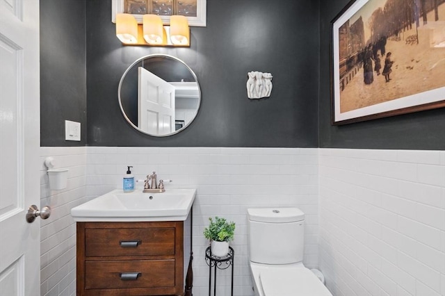 half bath featuring tile walls, wainscoting, toilet, and vanity