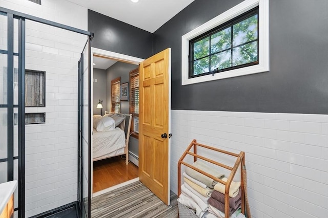 ensuite bathroom featuring connected bathroom, wood finished floors, a stall shower, and wainscoting