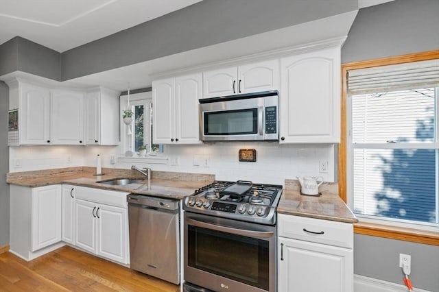 kitchen with light wood-style flooring, a sink, appliances with stainless steel finishes, white cabinetry, and tasteful backsplash