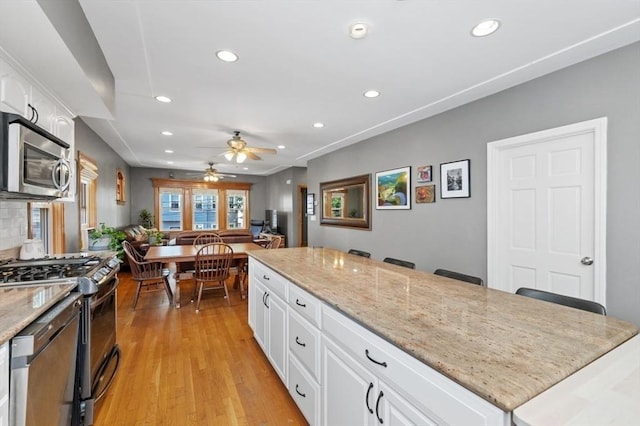 kitchen with light stone countertops, recessed lighting, appliances with stainless steel finishes, light wood-style floors, and white cabinets