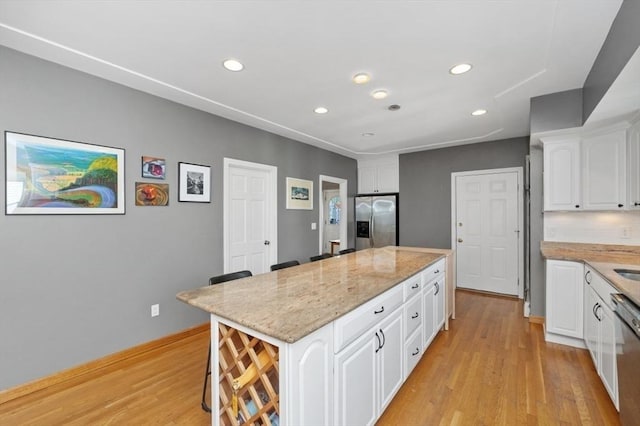 kitchen featuring light wood-style flooring, light stone counters, a center island, appliances with stainless steel finishes, and white cabinets