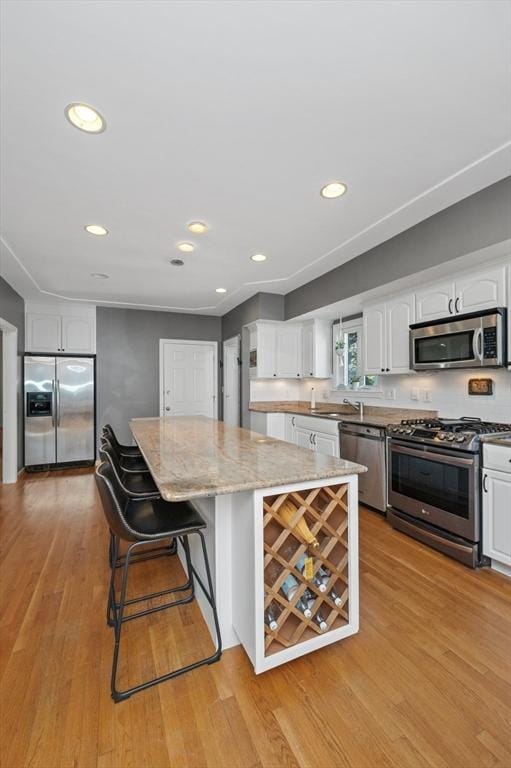 kitchen featuring light stone counters, a center island, white cabinetry, stainless steel appliances, and light wood finished floors