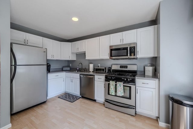 kitchen featuring stainless steel appliances, a sink, white cabinets, light wood-style flooring, and recessed lighting