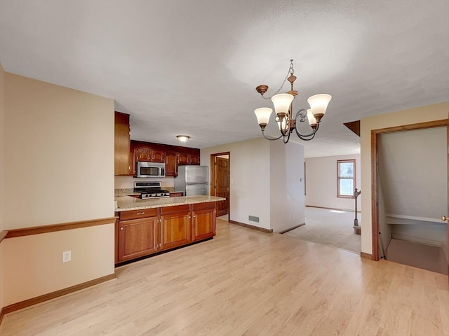 kitchen with an inviting chandelier, hanging light fixtures, light wood-type flooring, and appliances with stainless steel finishes