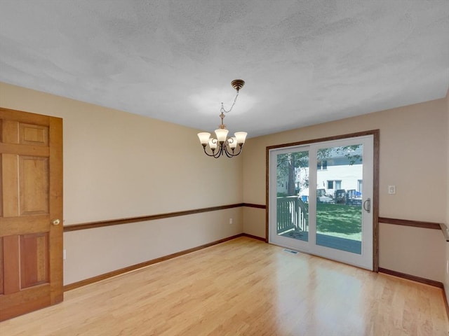 empty room with an inviting chandelier, a textured ceiling, and light wood-type flooring