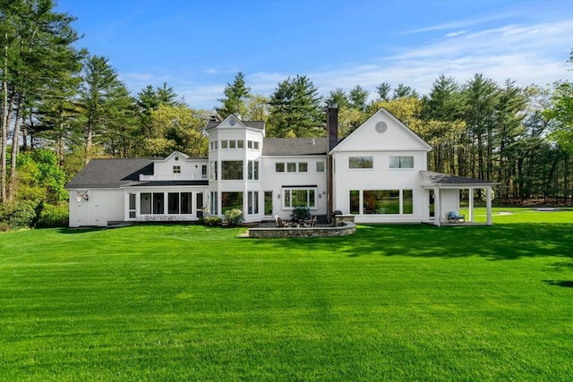 rear view of house with a yard, a chimney, a patio, and view of wooded area