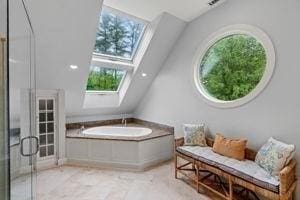 full bathroom with a skylight, plenty of natural light, vaulted ceiling, a shower with shower door, and a garden tub