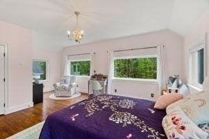 bedroom featuring a chandelier, wood finished floors, vaulted ceiling, and baseboards