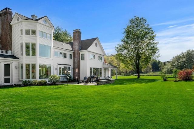 rear view of house featuring a yard, a patio, and a chimney