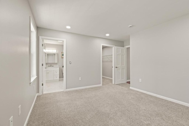 unfurnished bedroom with baseboards, recessed lighting, a walk in closet, and light carpet