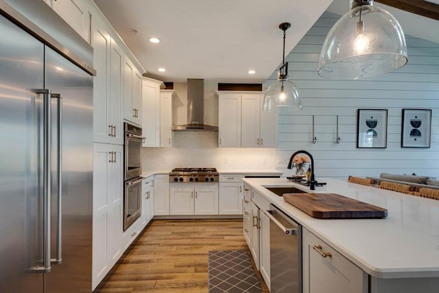 kitchen featuring light wood-type flooring, a sink, light countertops, stainless steel appliances, and wall chimney exhaust hood