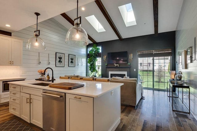 kitchen with white cabinets, a sink, vaulted ceiling with skylight, stainless steel dishwasher, and dark wood-style floors