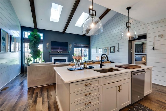 kitchen with vaulted ceiling with skylight, dark wood finished floors, a sink, open floor plan, and wooden walls