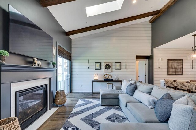 living area featuring dark wood-style flooring, high vaulted ceiling, beamed ceiling, a glass covered fireplace, and wooden walls
