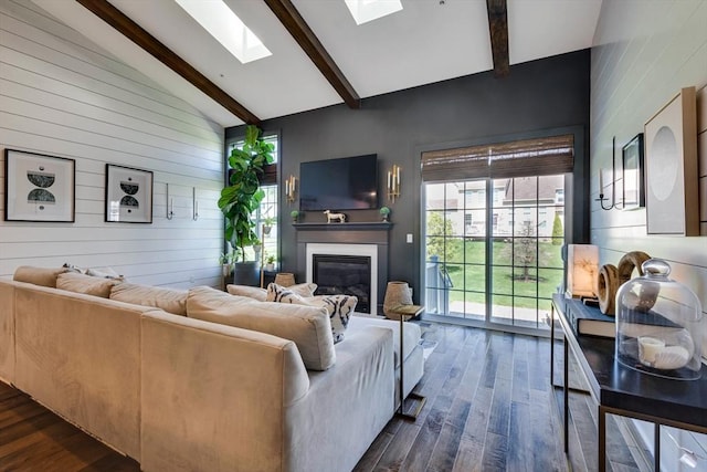 living area featuring wood walls, a glass covered fireplace, beamed ceiling, dark wood-type flooring, and a skylight
