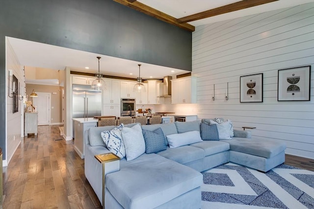 living room with a towering ceiling, wood walls, beam ceiling, recessed lighting, and hardwood / wood-style floors