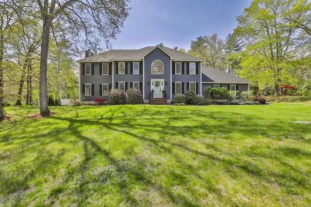 colonial house featuring a chimney, a front lawn, and entry steps