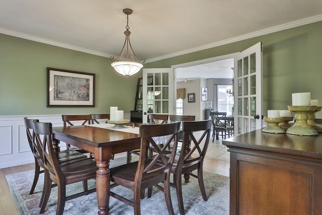 dining area with ornamental molding, french doors, light wood finished floors, and a wainscoted wall