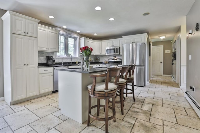 kitchen featuring stainless steel appliances, stone tile floors, baseboard heating, dark countertops, and tasteful backsplash