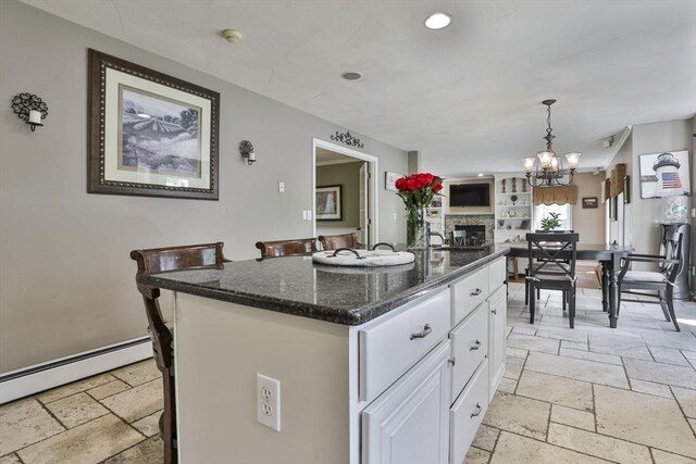 kitchen with stone tile flooring, a baseboard heating unit, white cabinets, dark stone counters, and a chandelier