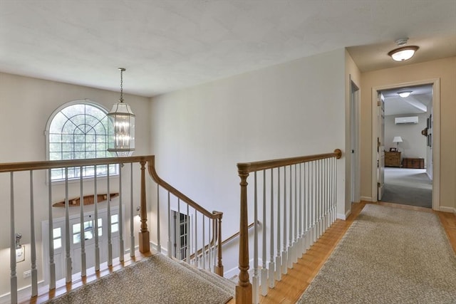 corridor with a chandelier, wood finished floors, baseboards, an upstairs landing, and a wall mounted AC
