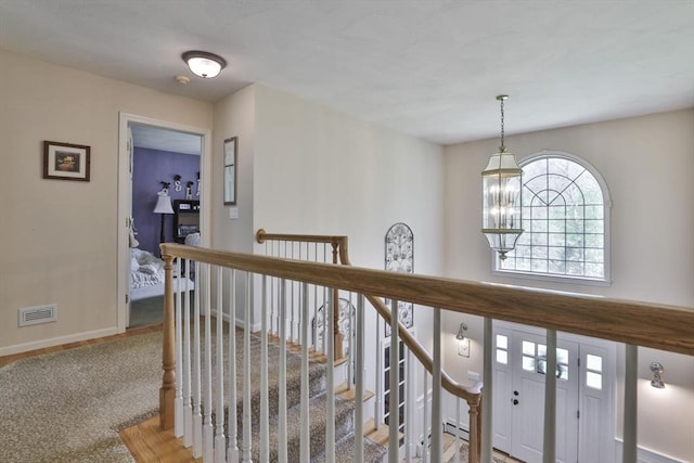 hallway with an upstairs landing, baseboards, and a chandelier