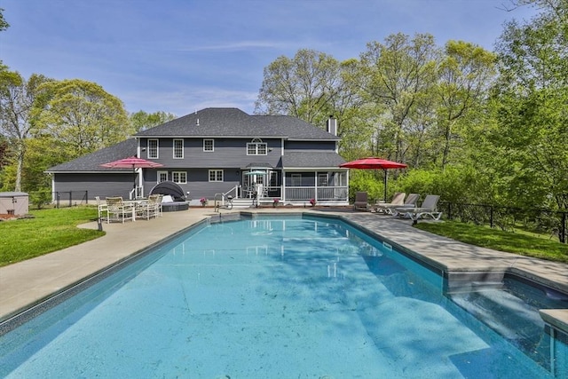 back of property with a sunroom, a patio area, and an outdoor pool