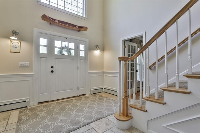 foyer entrance with a wainscoted wall, stone tile flooring, a decorative wall, a baseboard radiator, and stairway