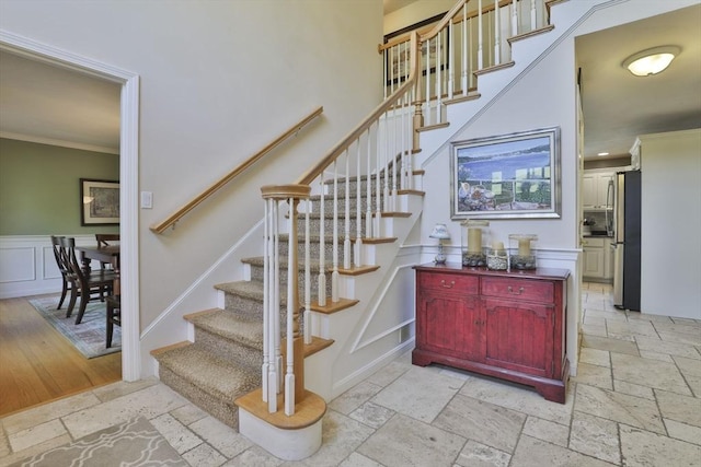 staircase featuring stone tile flooring, crown molding, a decorative wall, and wainscoting