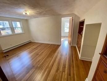 spare room featuring plenty of natural light, vaulted ceiling, wood-type flooring, and a baseboard heating unit