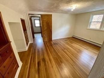 unfurnished room featuring baseboard heating, a healthy amount of sunlight, vaulted ceiling, and hardwood / wood-style flooring