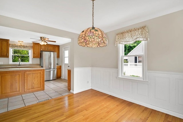 kitchen featuring freestanding refrigerator, wainscoting, brown cabinets, decorative light fixtures, and light countertops