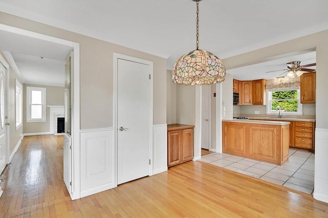 kitchen featuring light wood-type flooring, light countertops, a sink, crown molding, and decorative light fixtures