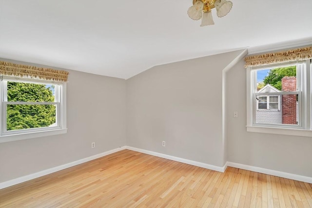 empty room featuring healthy amount of natural light, baseboards, light wood-style flooring, and vaulted ceiling