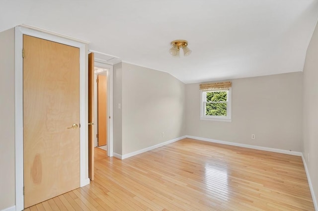 spare room with light wood finished floors, baseboards, and lofted ceiling