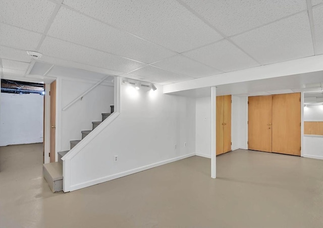 finished below grade area with a paneled ceiling, stairs, and baseboards