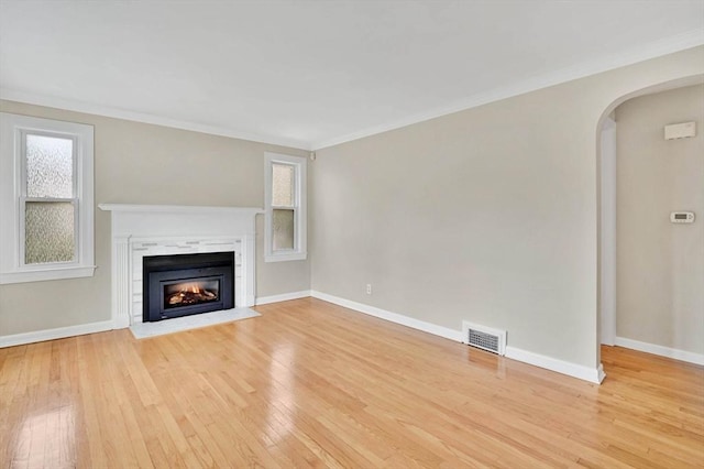 unfurnished living room with light wood finished floors, arched walkways, a glass covered fireplace, baseboards, and crown molding