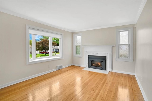 unfurnished living room with ornamental molding, plenty of natural light, light wood-style floors, a fireplace with flush hearth, and baseboards