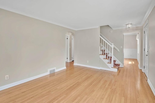 unfurnished living room featuring stairs, light wood-style flooring, ornamental molding, baseboards, and arched walkways