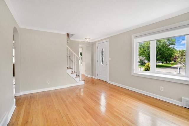 entryway with ornamental molding, arched walkways, light wood-style floors, stairs, and baseboards