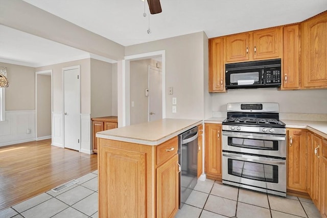 kitchen with stainless steel appliances, light countertops, a peninsula, light tile patterned flooring, and wainscoting