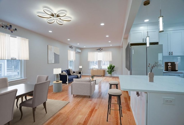 interior space featuring pendant lighting, a wall mounted air conditioner, light stone countertops, light hardwood / wood-style floors, and a breakfast bar area